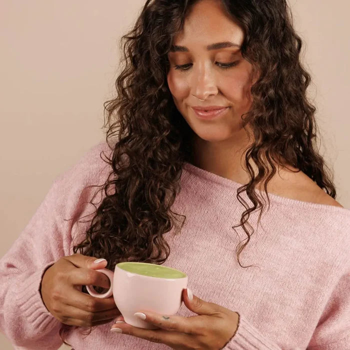 Woman holding a pink mug with green strawberry matcha latte.